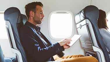 Ein Mann im Flugzeug hat ein Tablet in der Hand und tippt darauf herum