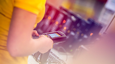 Eine weibliche Hand hält in einem Lager ein mobiles Scangerät in der Hand