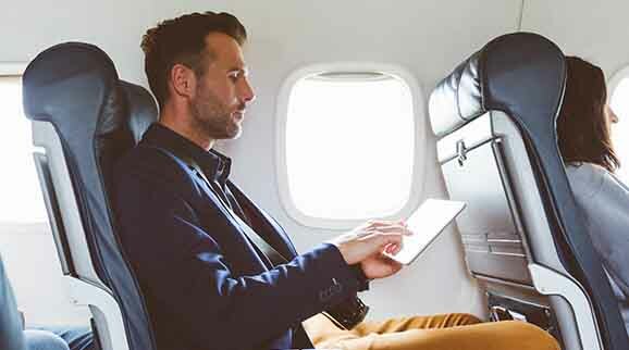 Ein Mann im Flugzeugsitz während er ein iPad (ein Produkt der Firma Apple) bedient