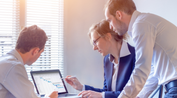 Drei Personen die auf einen Laptopbildschirm schauen das Projektmanagement analysieren