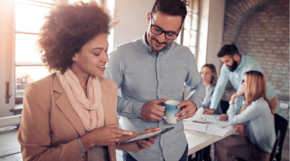 Projektmanagement Plan bei dem ein Mann und eine Frau nebeneinander stehen und auf ein Tablet schauen