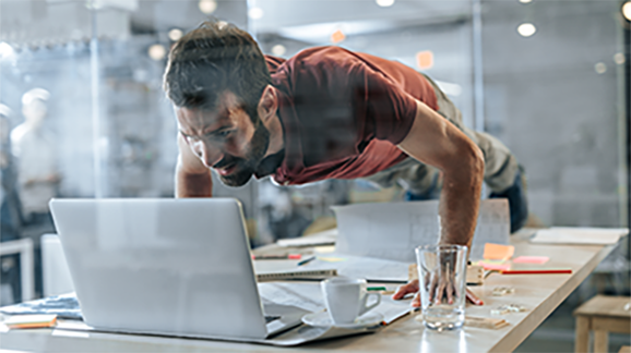 Rethink Business Processes während ein Mann auf einem Tisch gut gelaunt vor seinem Laptop Liegestützen macht