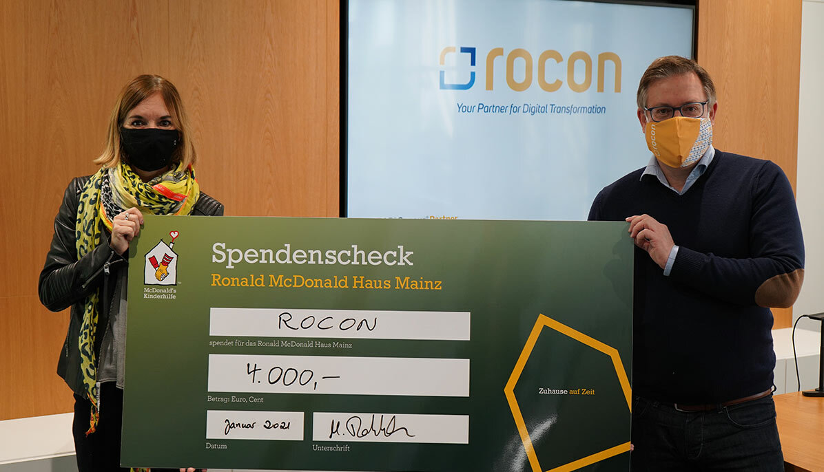 Zwei Rocon Angestellte halten zu zweit einen Check für die Kinderhilfe Spendenübergabe bei McDonalds