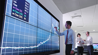 Ein Mann vor einem riesigen Bildschirm auf dem ein Performance Verlauf digital dargestellt wird