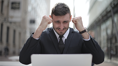 Ein Mann vor einem Laptop freut sich mit den Fäusten in den Himmel streckend