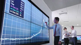 Ein Mann vor einem riesigen Bildschirm auf dem ein Performance Verlauf digital dargestellt wird