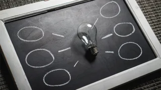 "Great Idea" dargestellt mit einer Glühbirne liegend auf einer Tafel auf der Linien und Kreise von der Glühbirne abgebildet sind