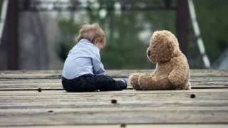 Sitzendes Baby mit einem gegenüber sitzendem Braunen Teddy auf einer Holzbrücke